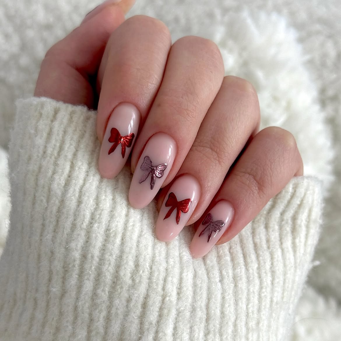 Glossy Nude Almond Nails With Metallic Red Bows